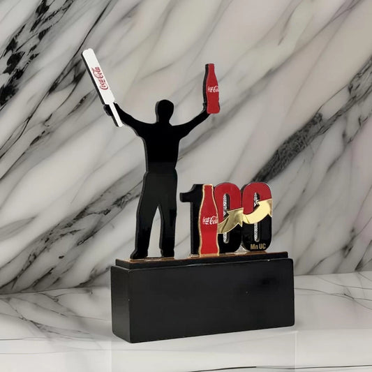 Milestone trophy of a batsman holding a bat and coca cola bottle, with 100 next to him