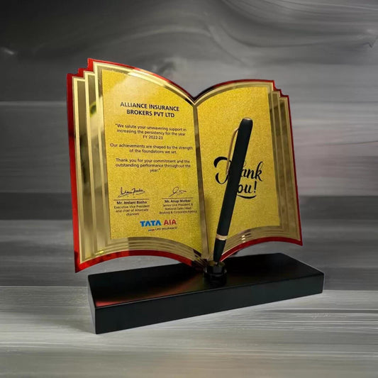 A golden and burgundy thank you plaque in the shape of an open book with a pen in the front